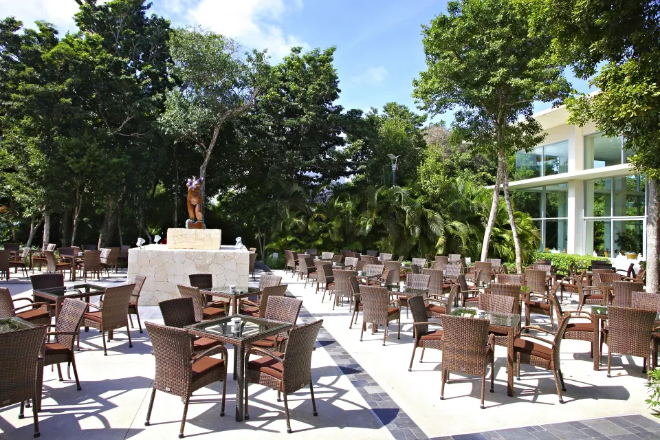 Outdoor terrace with many wicker tables and a central stone fountain at Bahia Principe Luxury Sian Ka'an