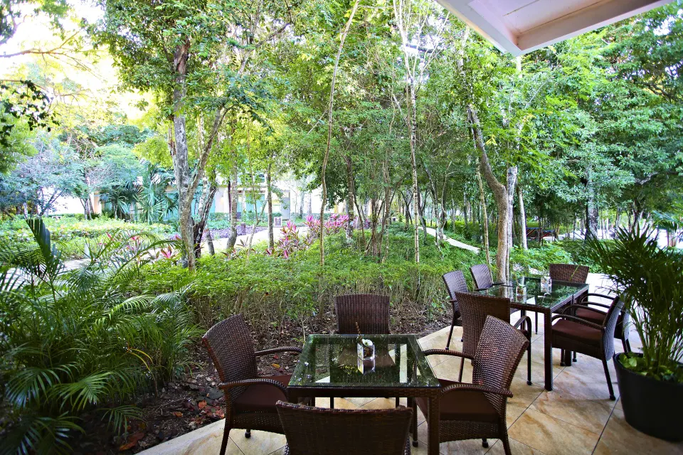 Shaded patio seating overlooking gardens with wicker tables at Bahia Principe Luxury Sian Ka'an