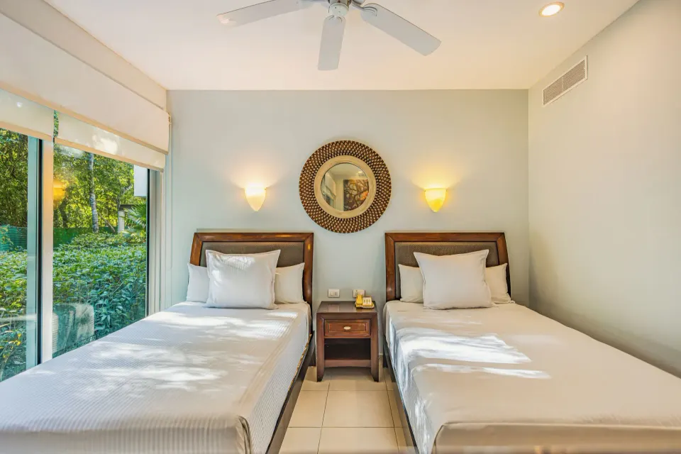 Two double beds with bedside table and leafy window view in junior suite at Bahia Principe Luxury Sian Ka'an