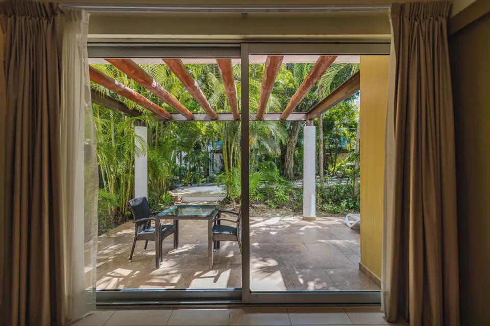 View through sliding doors to a shaded garden terrace from a Junior Suite at Bahia Principe Luxury Sian Ka'an