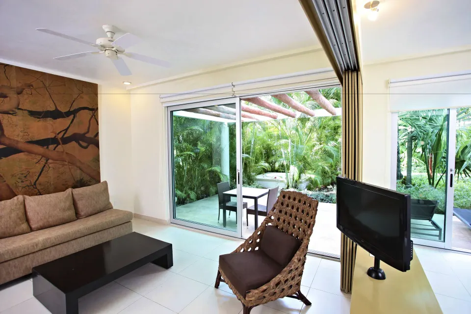 Sitting area with wicker chair and patio beyond sliding doors at Bahia Principe Luxury Sian Ka'an