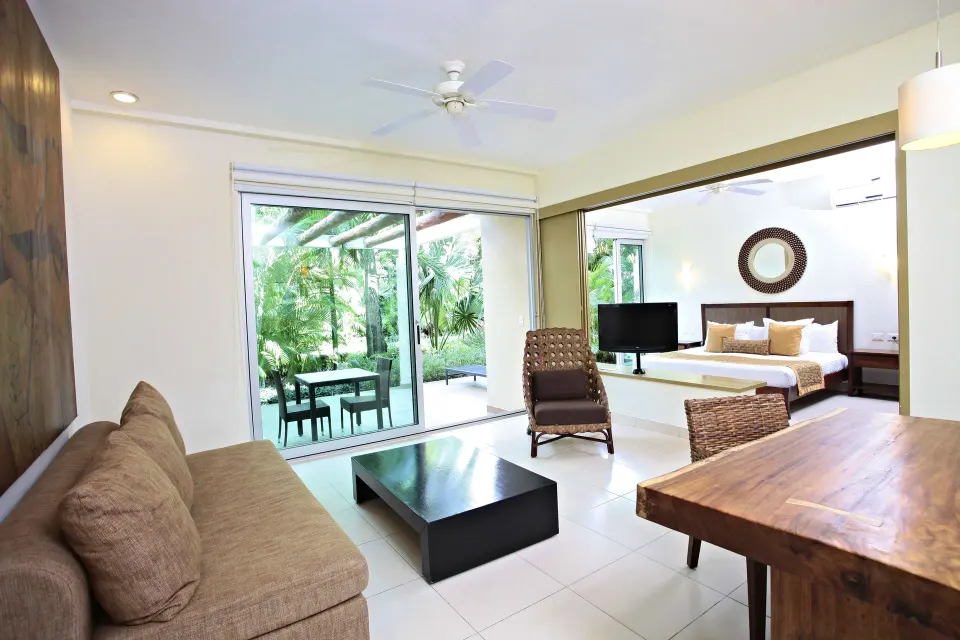 Living area and king bed seen through room divider with patio beyond at Bahia Principe Luxury Sian Ka'an