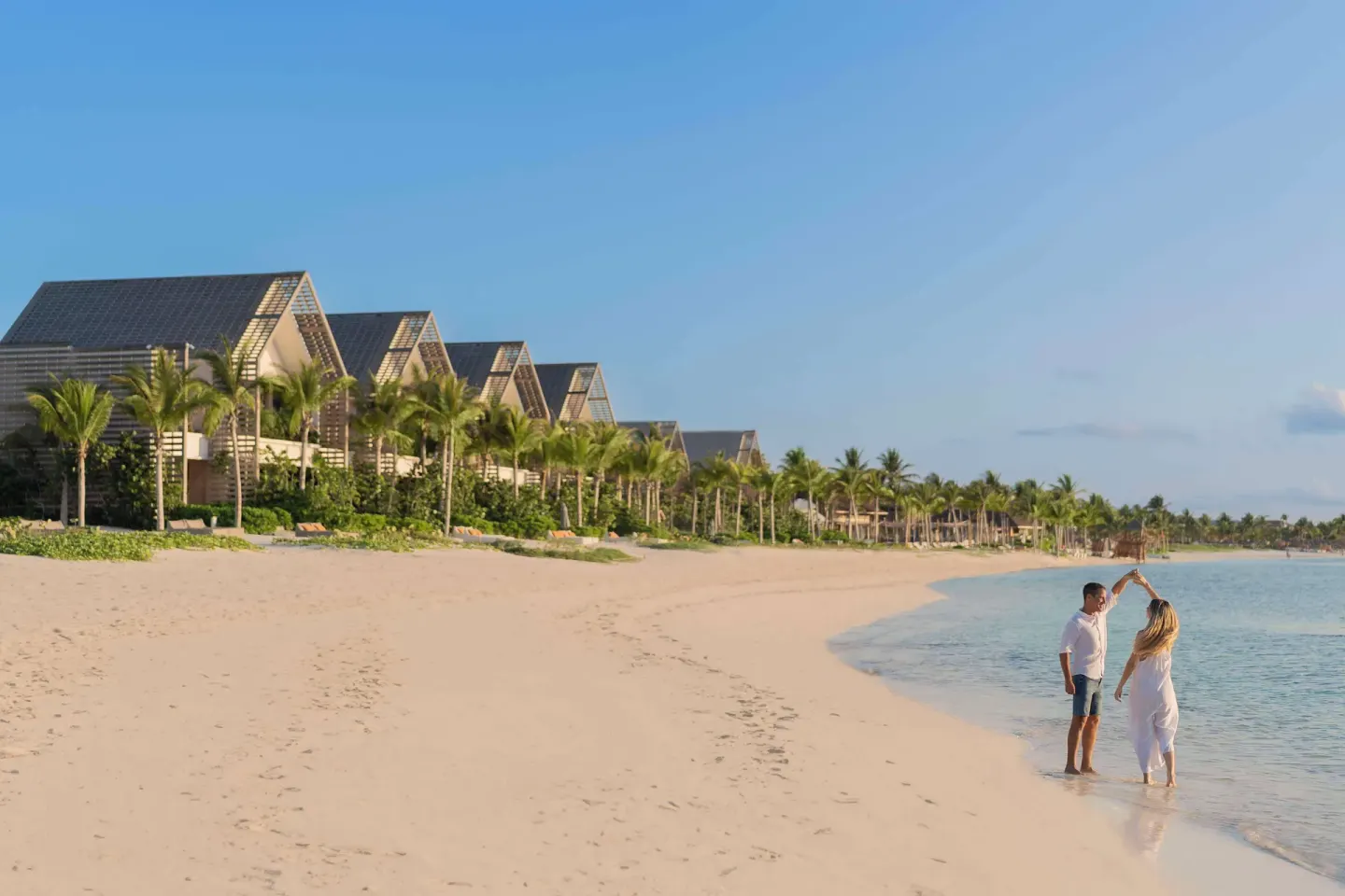 Beachfront with calm water, palm trees and resort buildings at Banyan Tree Mayakoba.