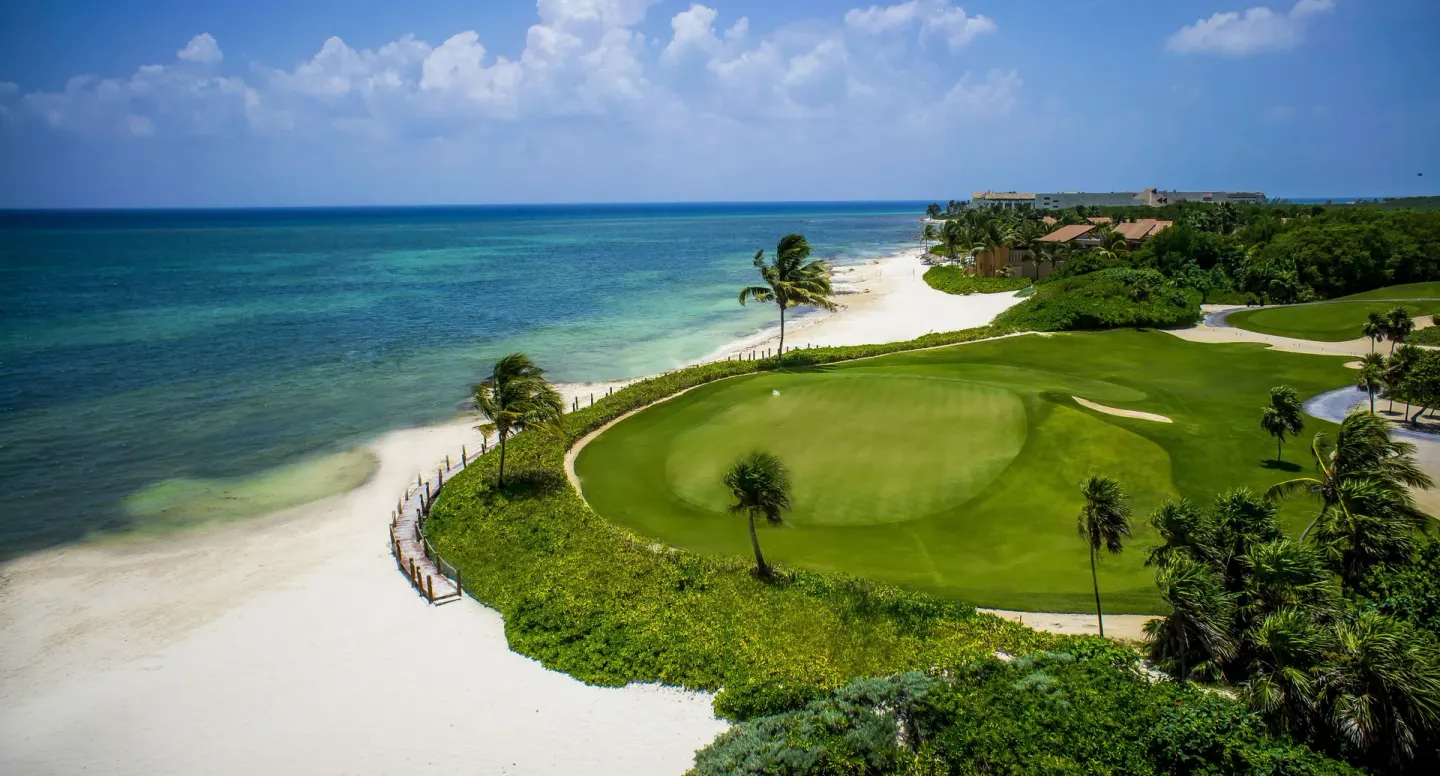Aerial view of a coastal golf green beside turquoise water at Banyan Tree Mayakoba.