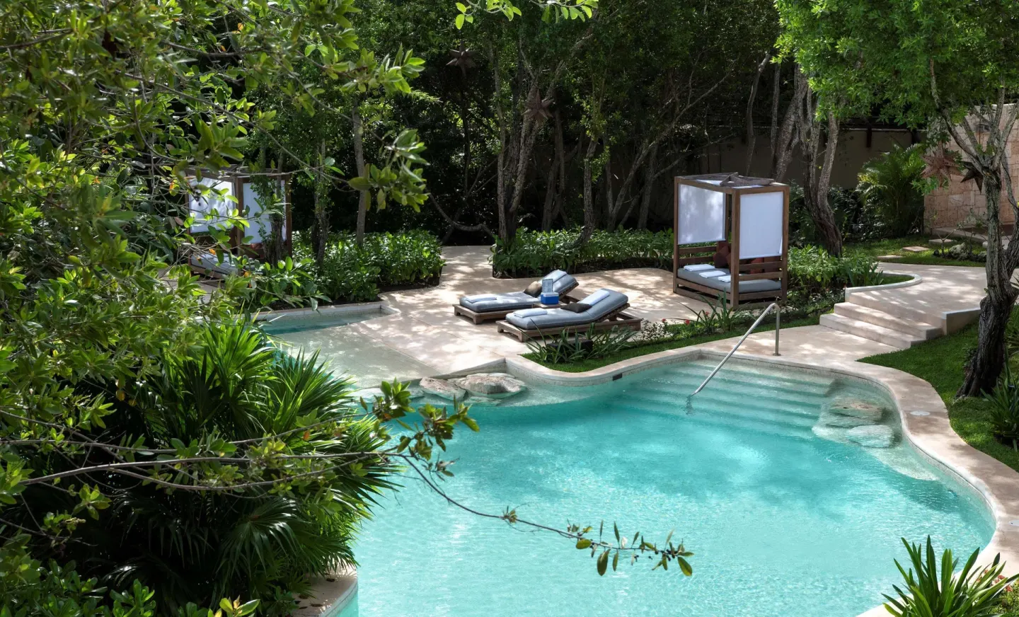 Curved outdoor pool with loungers and cabana among trees at Banyan Tree Mayakoba.