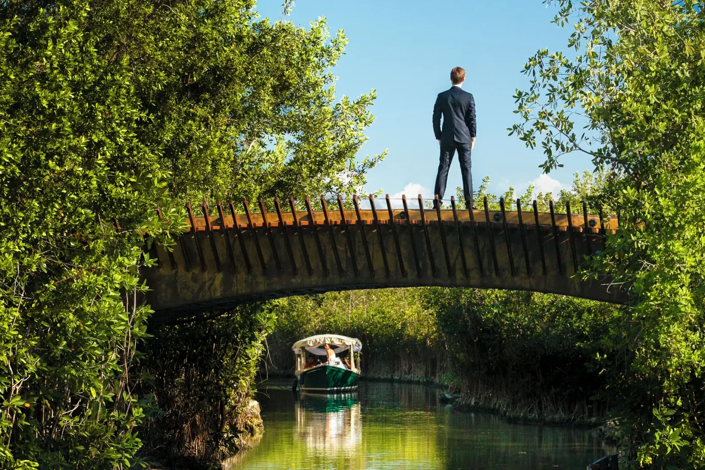 A guest stands on a canal bridge as a boat passes through mangroves at Banyan Tree Mayakoba.