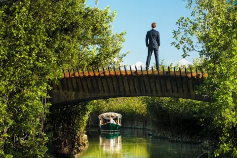 A guest stands on a canal bridge as a boat passes through mangroves at Banyan Tree Mayakoba.