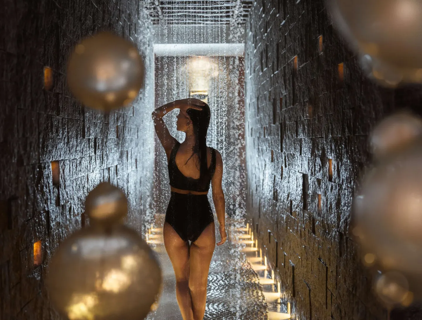 Guest under a rainfall shower in a stone spa corridor at Banyan Tree Mayakoba.