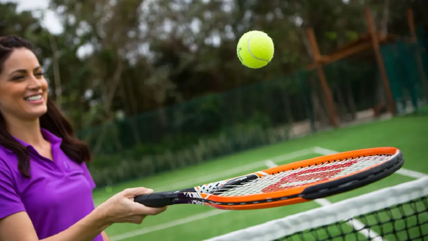 A smiling tennis player balances a ball on a racket at Banyan Tree Mayakoba.
