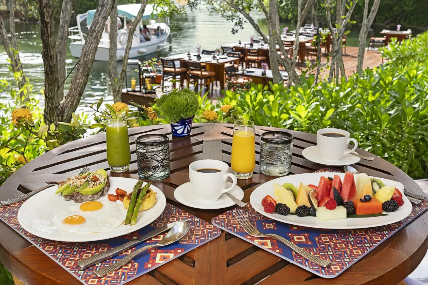Breakfast plates with fruit, eggs, juice and coffee beside the lagoon at Banyan Tree Mayakoba.