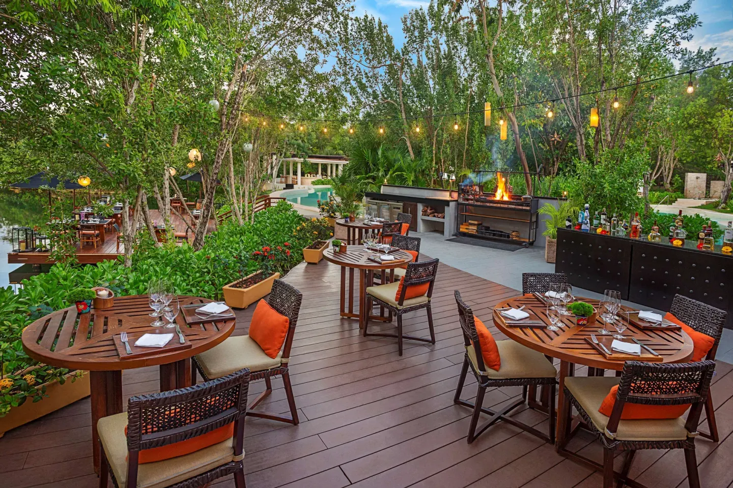 Open-air grill terrace with set tables among trees at Banyan Tree Mayakoba.