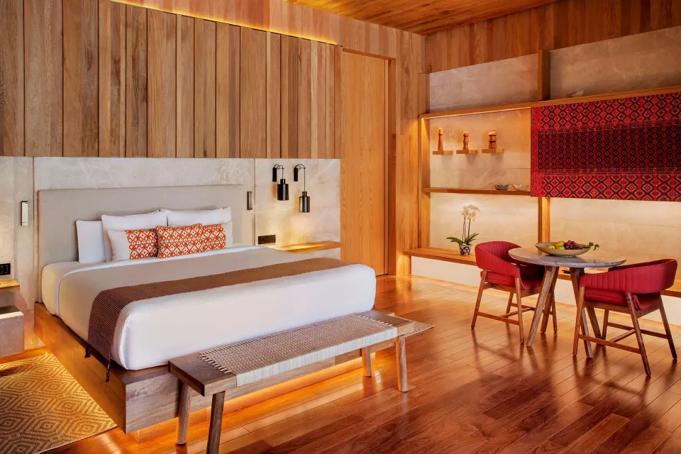 Beachfront Lanai Pool Suite king bed at Banyan Tree Mayakoba with dining table and wood interiors.