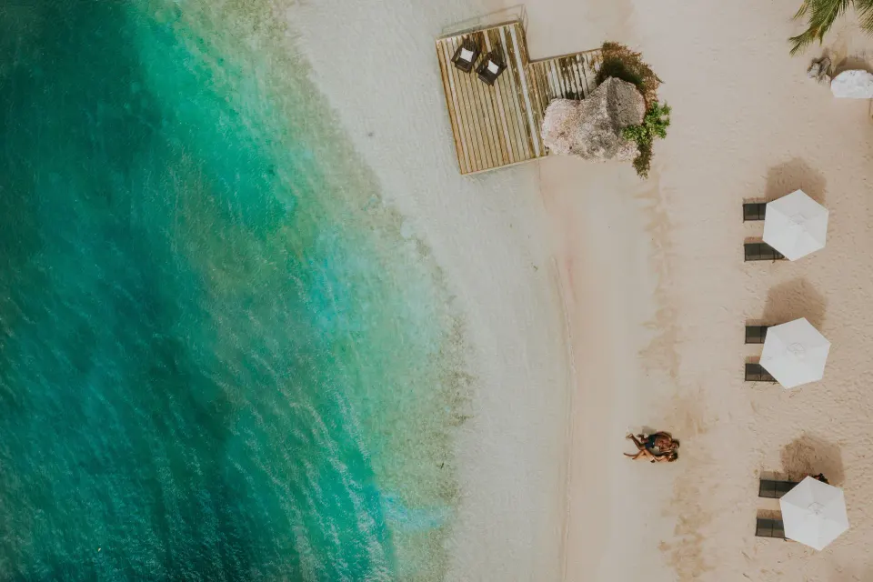 Aerial view of a sandy beach with turquoise water and sun umbrellas at Baoase Luxury Resort.