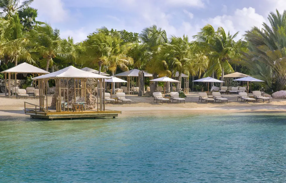 Rows of beach loungers and umbrellas beside turquoise water at Baoase Luxury Resort.