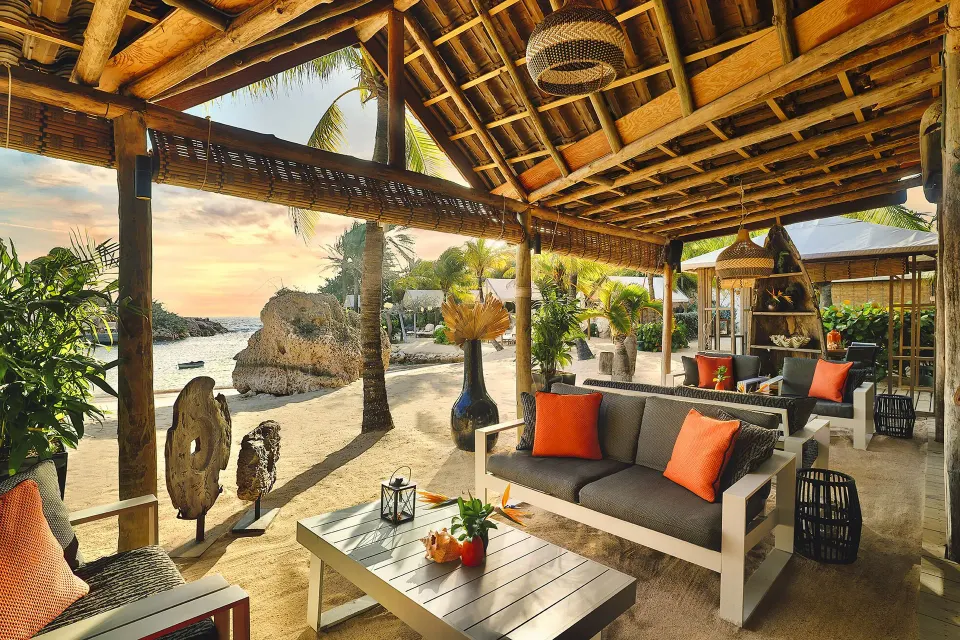 Shaded beachfront lounge with sofas and orange cushions at Baoase Luxury Resort