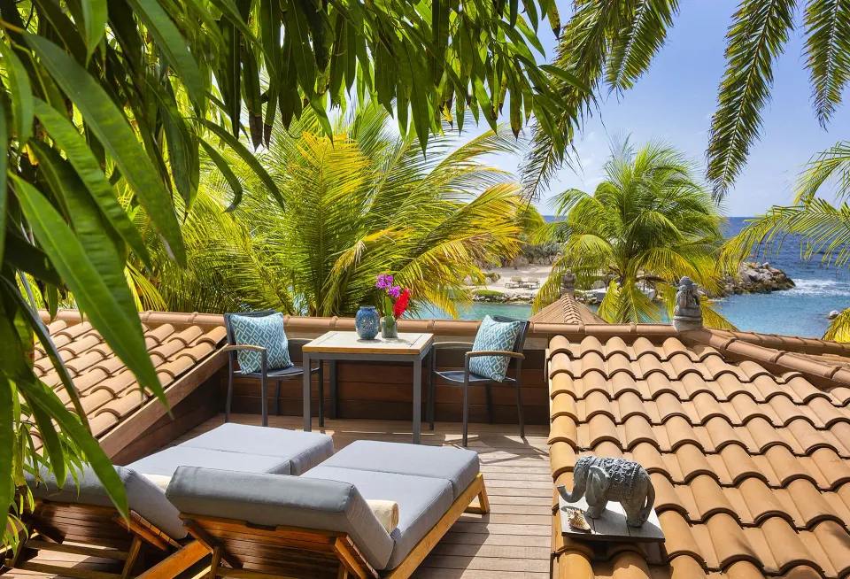Rooftop deck with twin daybeds and table overlooking palms and the sea at Baoase Luxury Resort