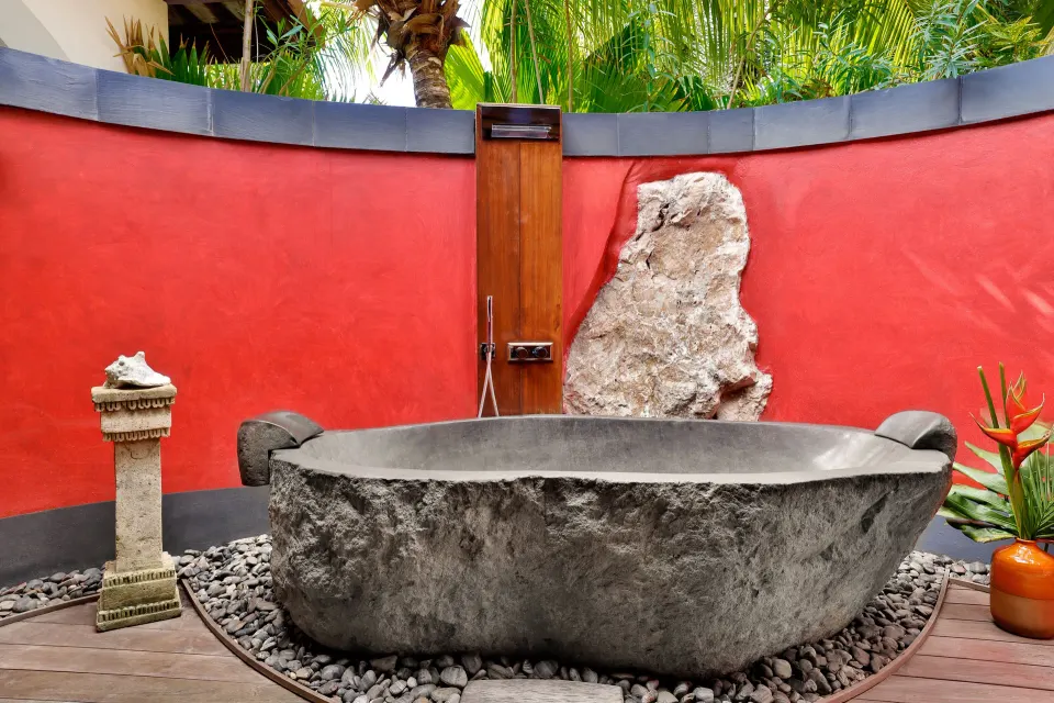 Stone freestanding bathtub with red wall in an outdoor villa area at Baoase Luxury Resort