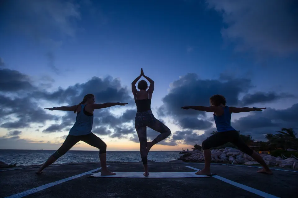 Silhouetted group practicing yoga on a seaside platform at Baoase Luxury Resort.