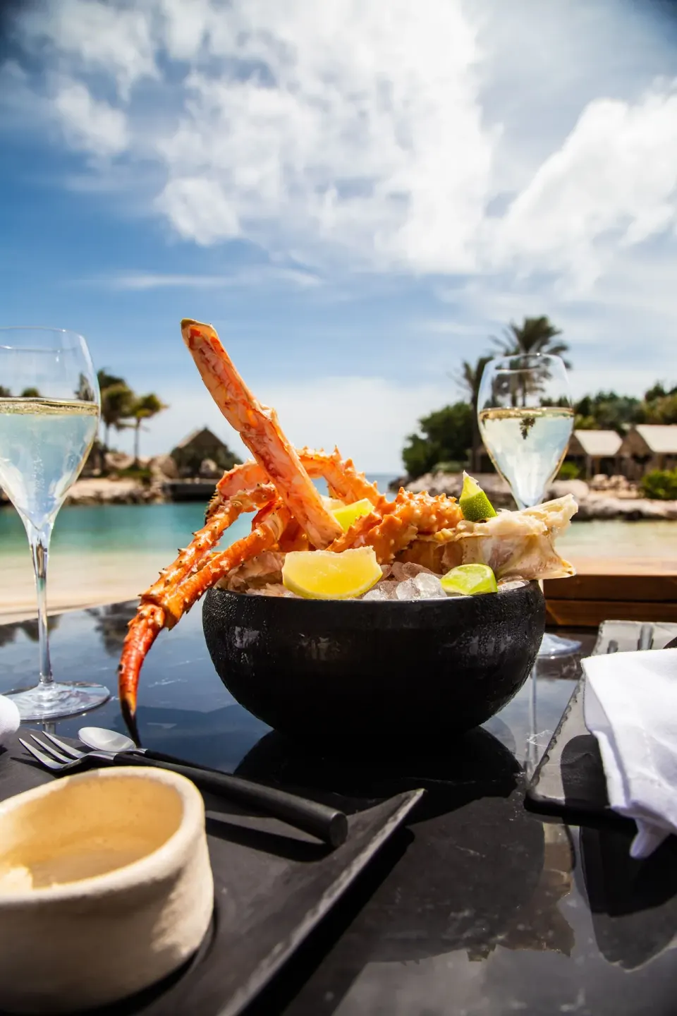 Bowl of chilled crab legs and lime with water and beach in background at Baoase Luxury Resort