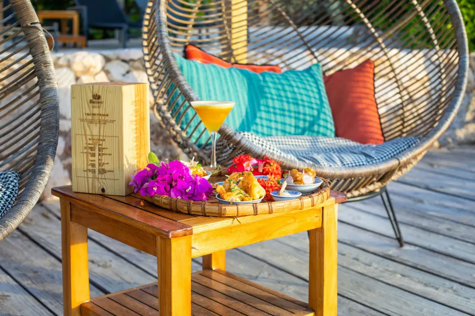 Small side table with cocktail, snacks and woven chairs on a deck at Baoase Luxury Resort