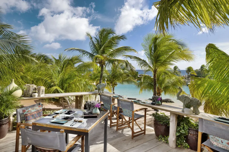 Oceanfront dining terrace with tables and palm trees overlooking the beach at Baoase Luxury Resort