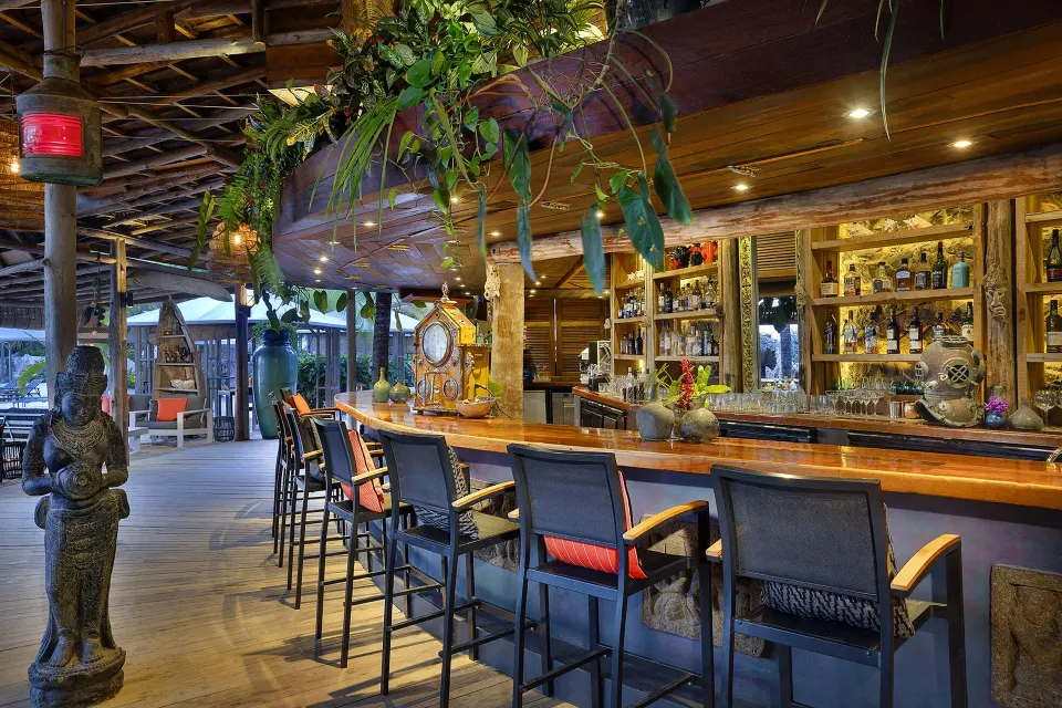 Wooden bar counter and stools under a tropical roof at Baoase Luxury Resort