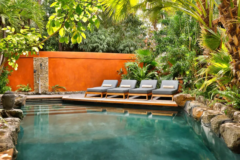 Private pool with sun loungers beside orange garden wall at Baoase Luxury Resort