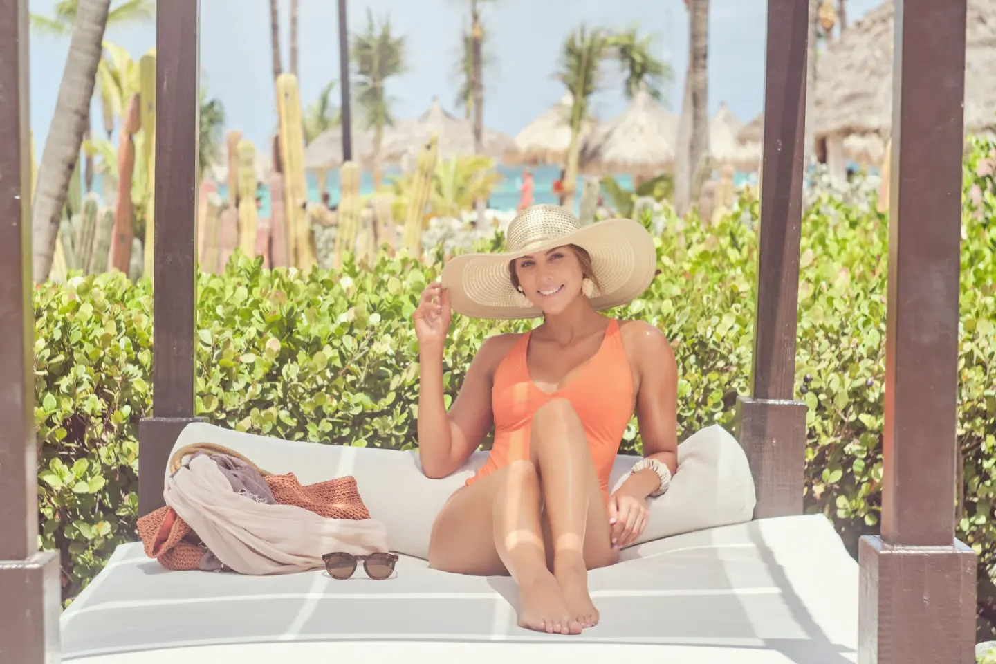 Guest relaxing on a shaded beach cabana with palms behind at Barceló Aruba.