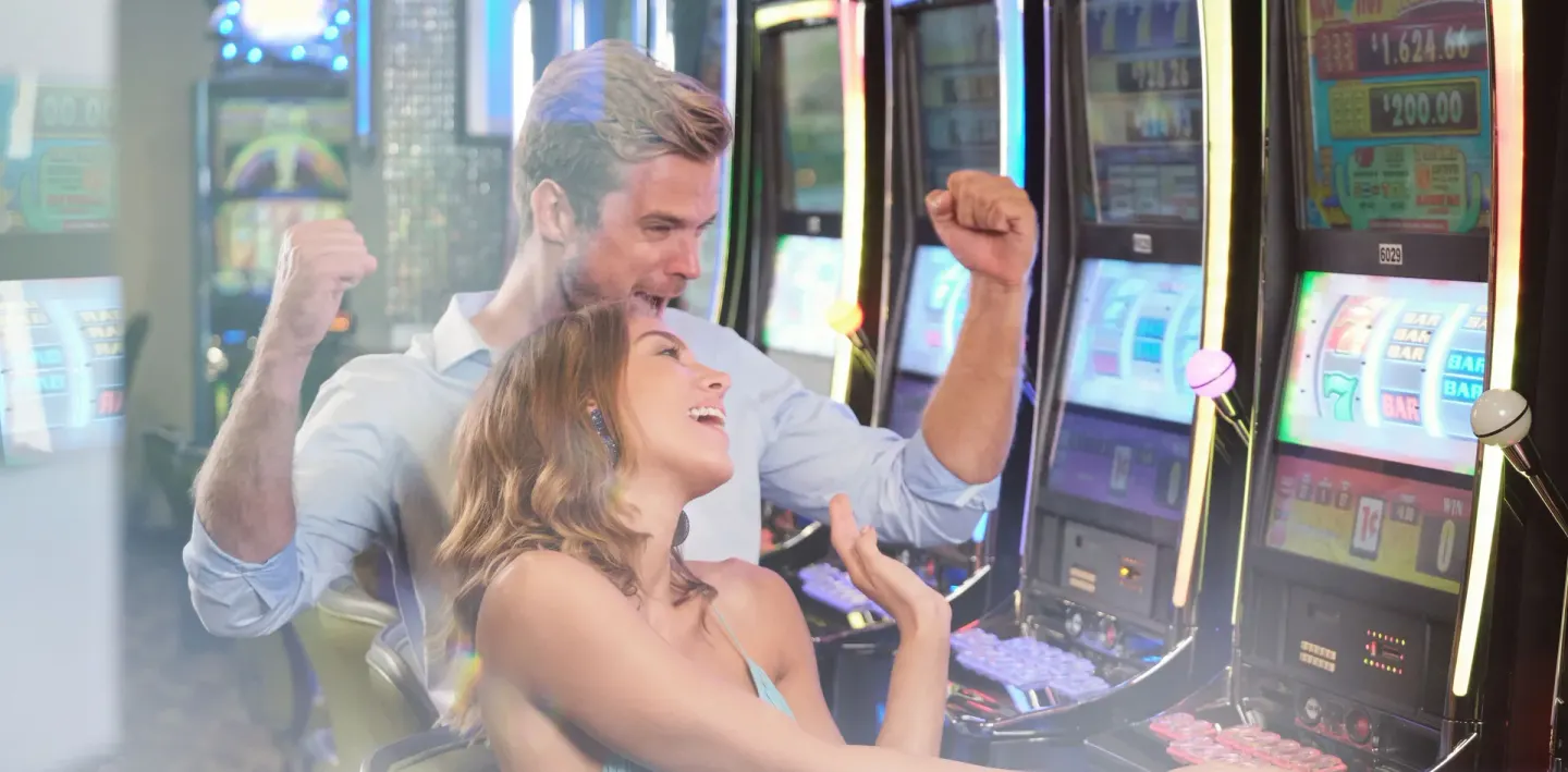 Two guests celebrating beside slot machines in the casino at Barceló Aruba.
