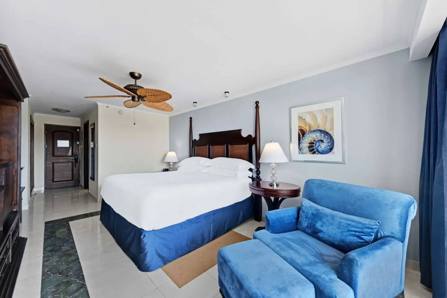 King bed guest room with blue armchair and dark wood furniture at Barceló Aruba.