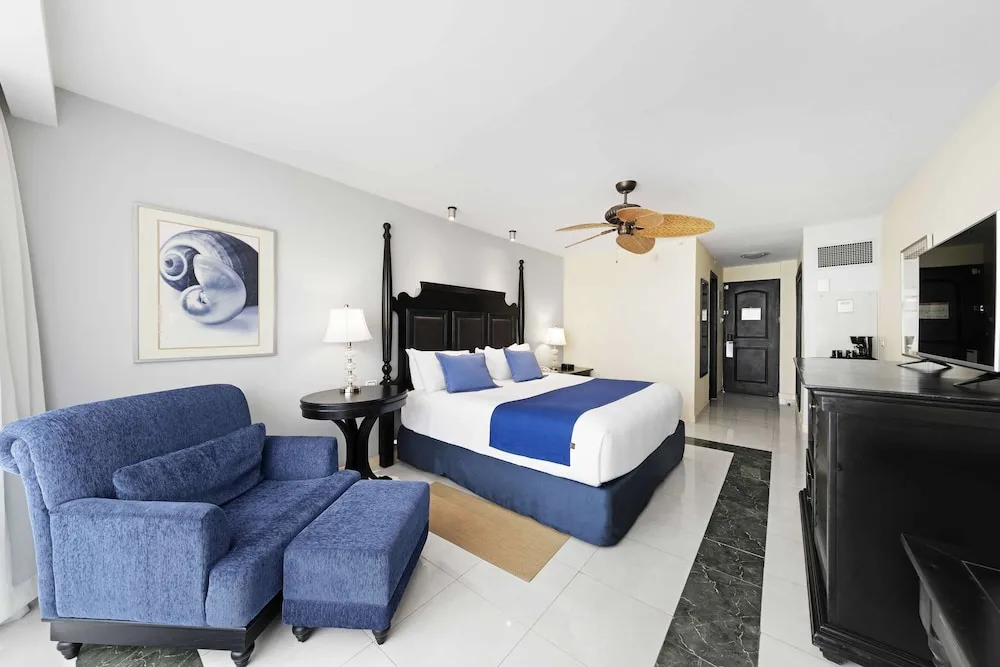King bed guest room with blue seating and dark wood furniture at Barceló Aruba.