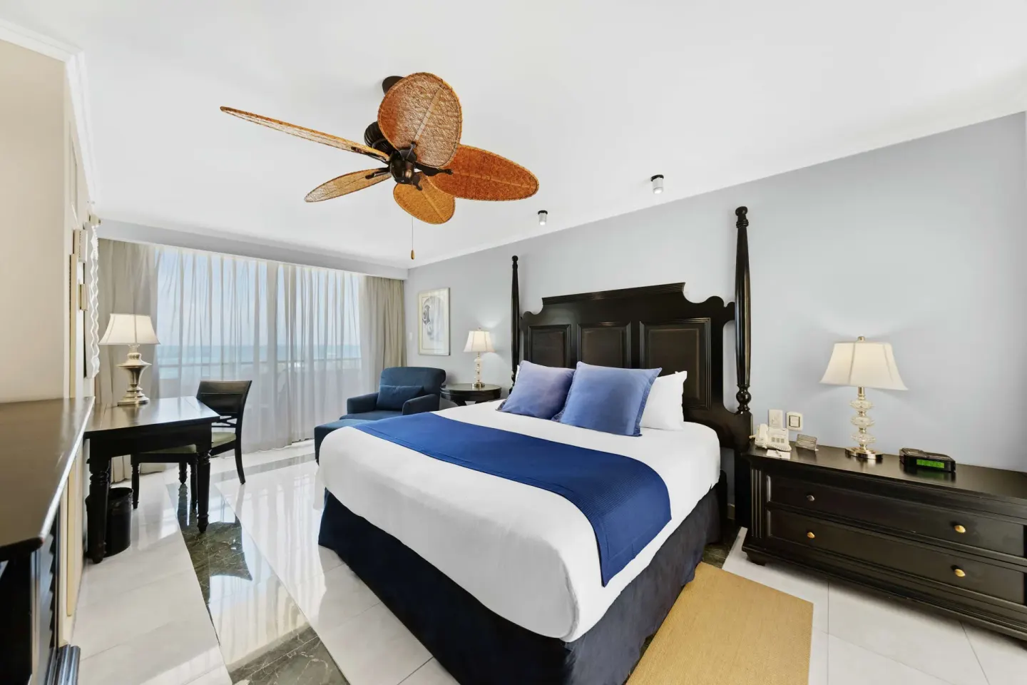 King bed guest room with desk, balcony curtains, and blue accents at Barceló Aruba.