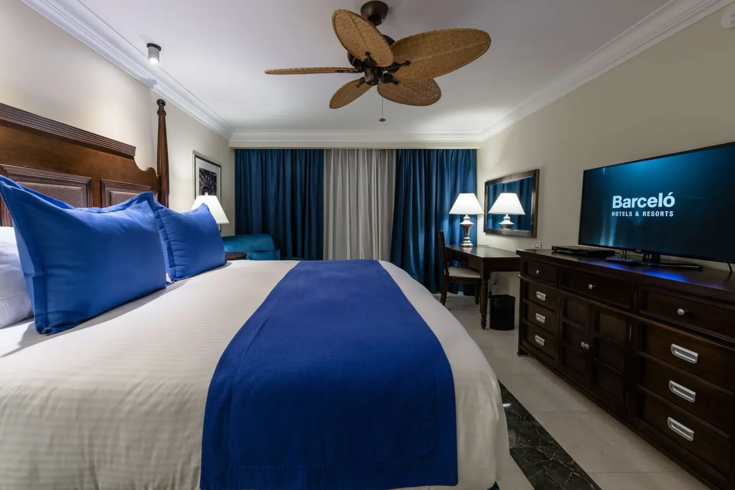 King bed guest room with TV, desk, and blue curtains at Barceló Aruba.