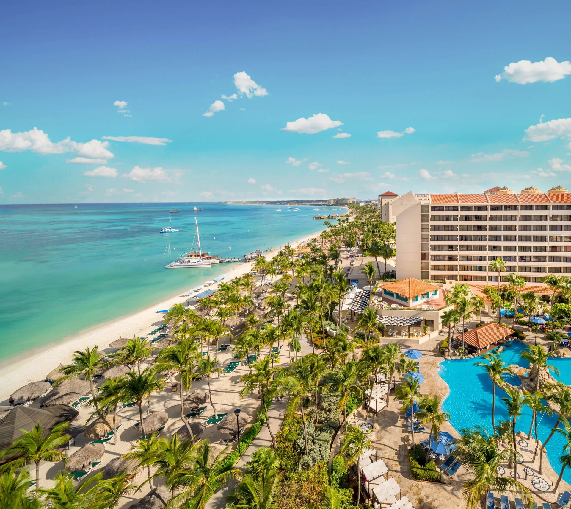 High view of the beach, pool, palms and resort tower at Barceló Aruba.