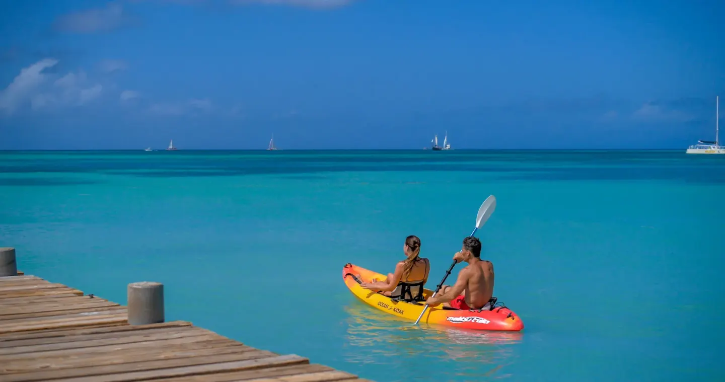 Two guests kayaking on turquoise water near a wooden pier at Barceló Aruba.