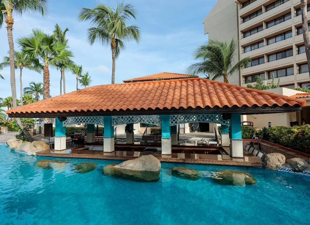 Closer view of the poolside pavilion with palms and hotel rooms at Barceló Aruba.