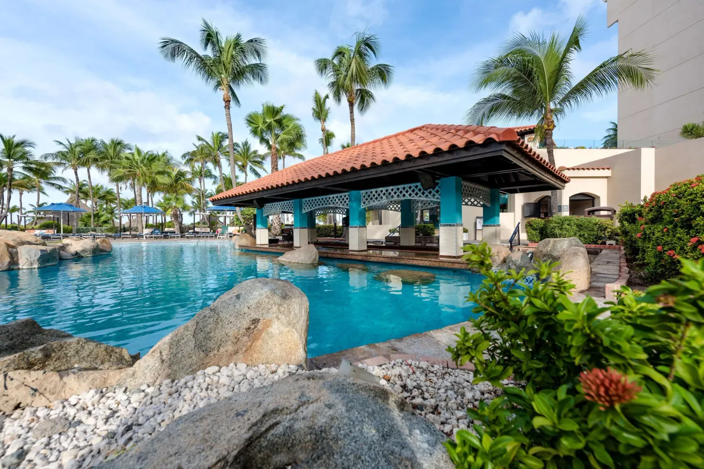 Poolside pavilion with red tile roof and palm trees at Barceló Aruba.