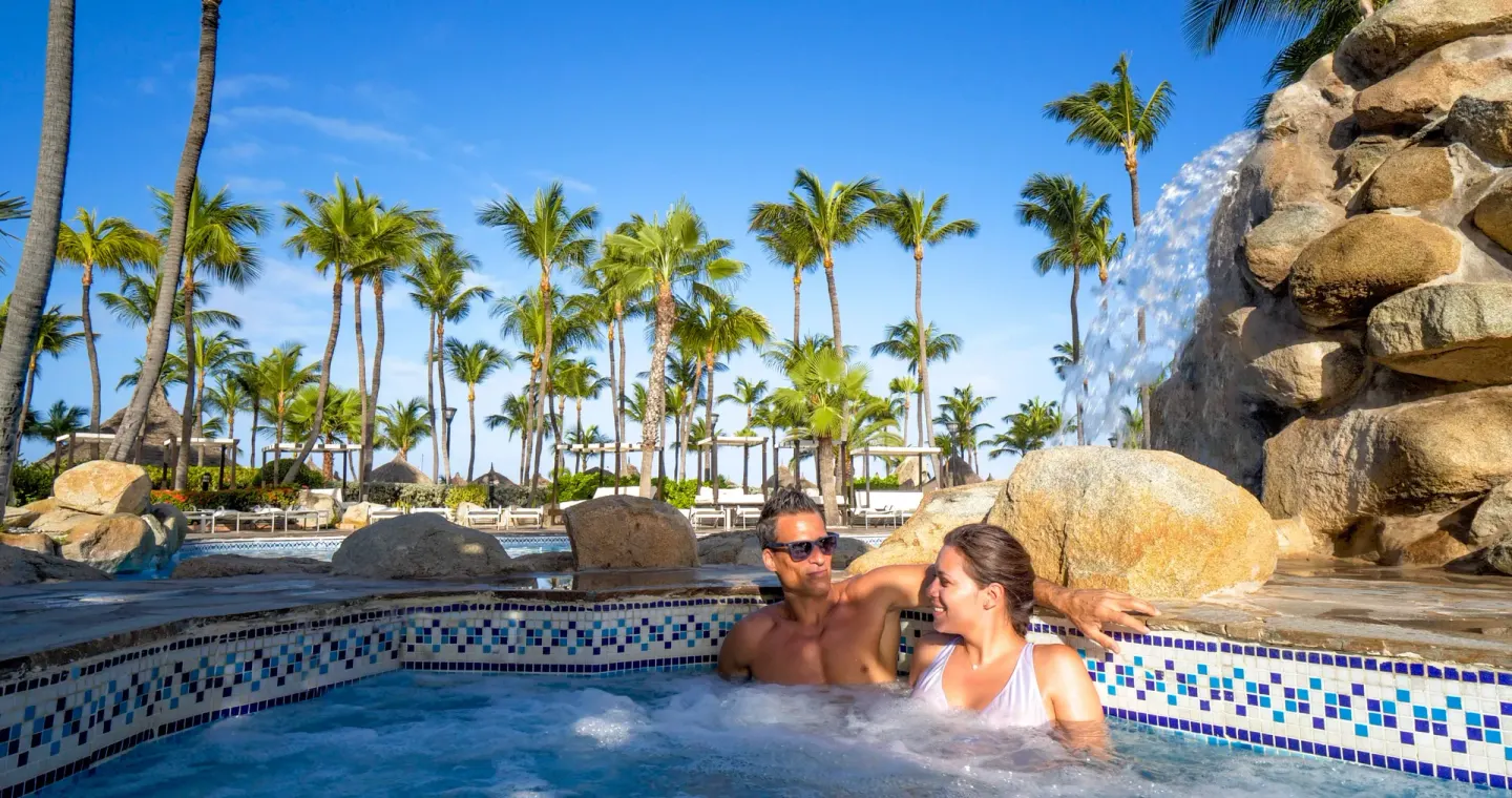 Couple relaxing in a bubbling pool beside a rock waterfall at Barceló Aruba.