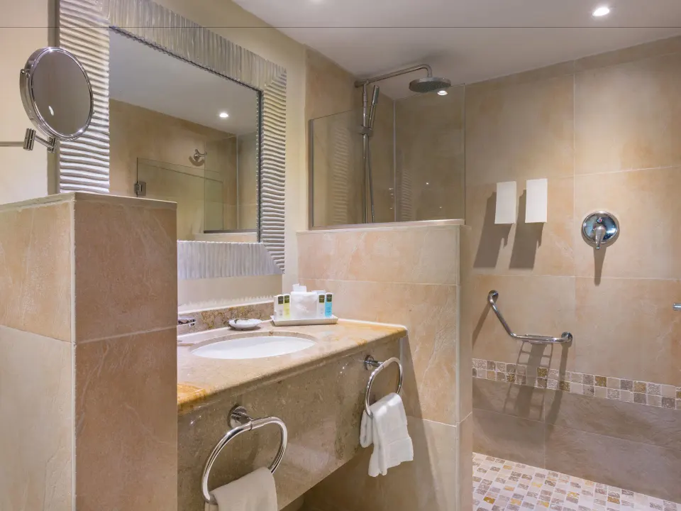 Deluxe Room bathroom with vanity, mirror, and glass shower at Barceló Aruba.