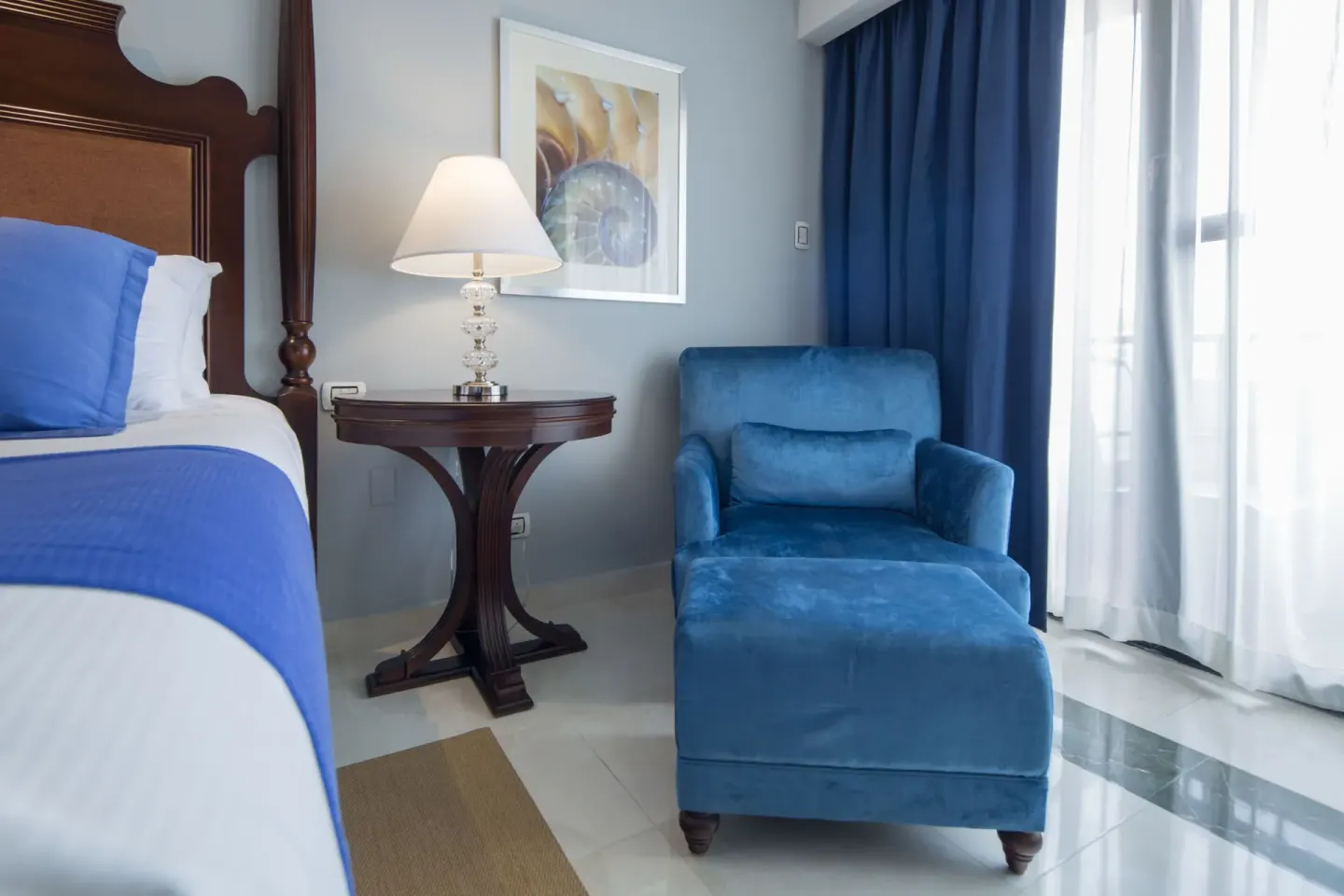 Deluxe Room bed and blue lounge chair beside the window at Barceló Aruba.