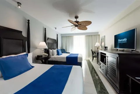 Deluxe Room with two beds, blue accents, TV console, and ceiling fan at Barceló Aruba.
