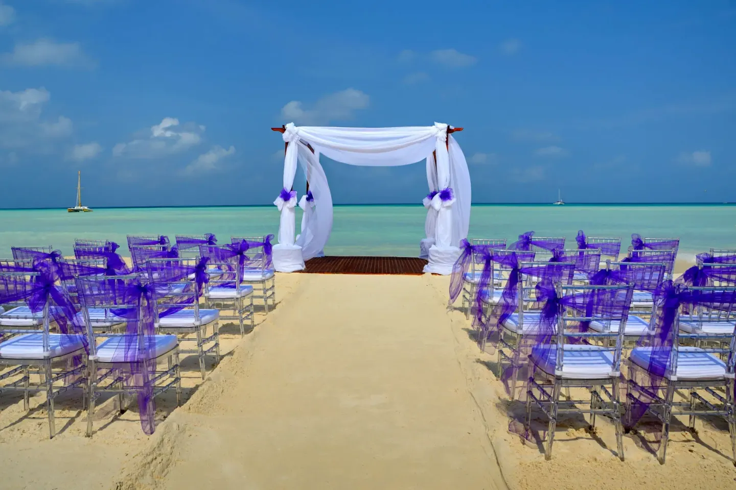 Beach wedding setup with white canopy and purple chair sashes at Barceló Aruba.