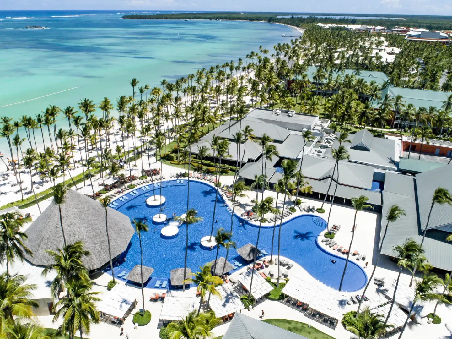 Curving pool, palms, beach loungers, and turquoise sea at Barceló Bávaro Beach.