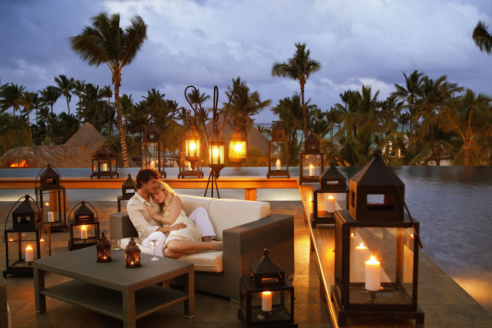 Couple seated by an infinity pool with candle lanterns at Barceló Bávaro Palace.