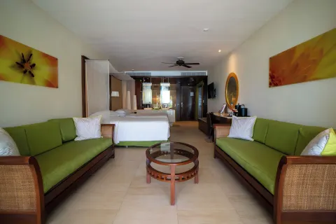 Guest room seating area with green sofas, glass table, and bed beyond at Barceló Bávaro Palace.