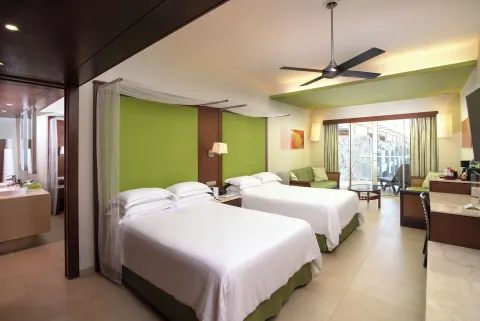 Guest room with two double beds, green accents, sofa, desk, and balcony at Barceló Bávaro Palace.