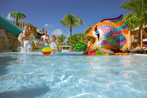 Family plays in the kids' pool with a fish slide at Barceló Bávaro Palace.