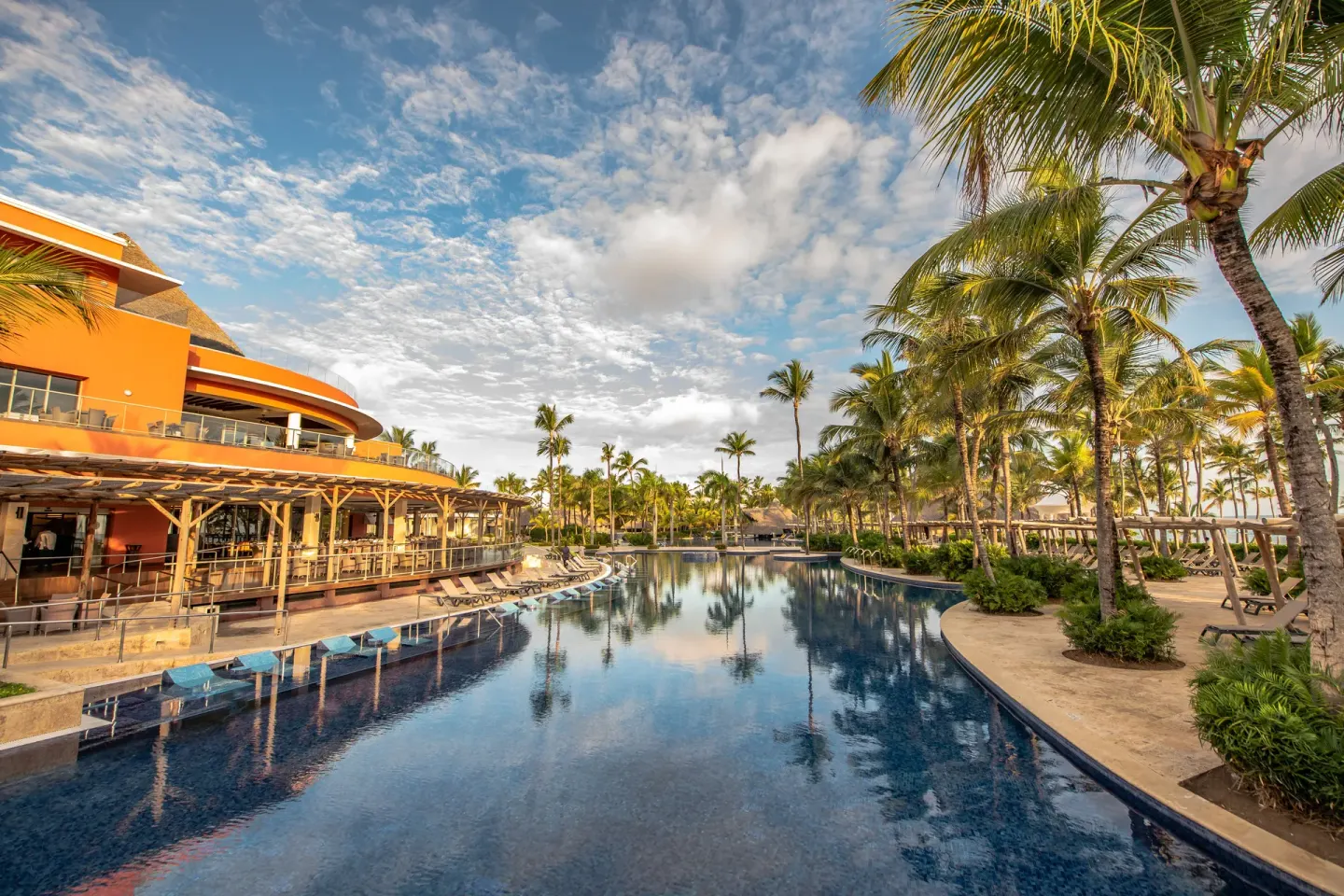 Long resort pool beside orange buildings, loungers, and palm trees at Barceló Bávaro Palace.