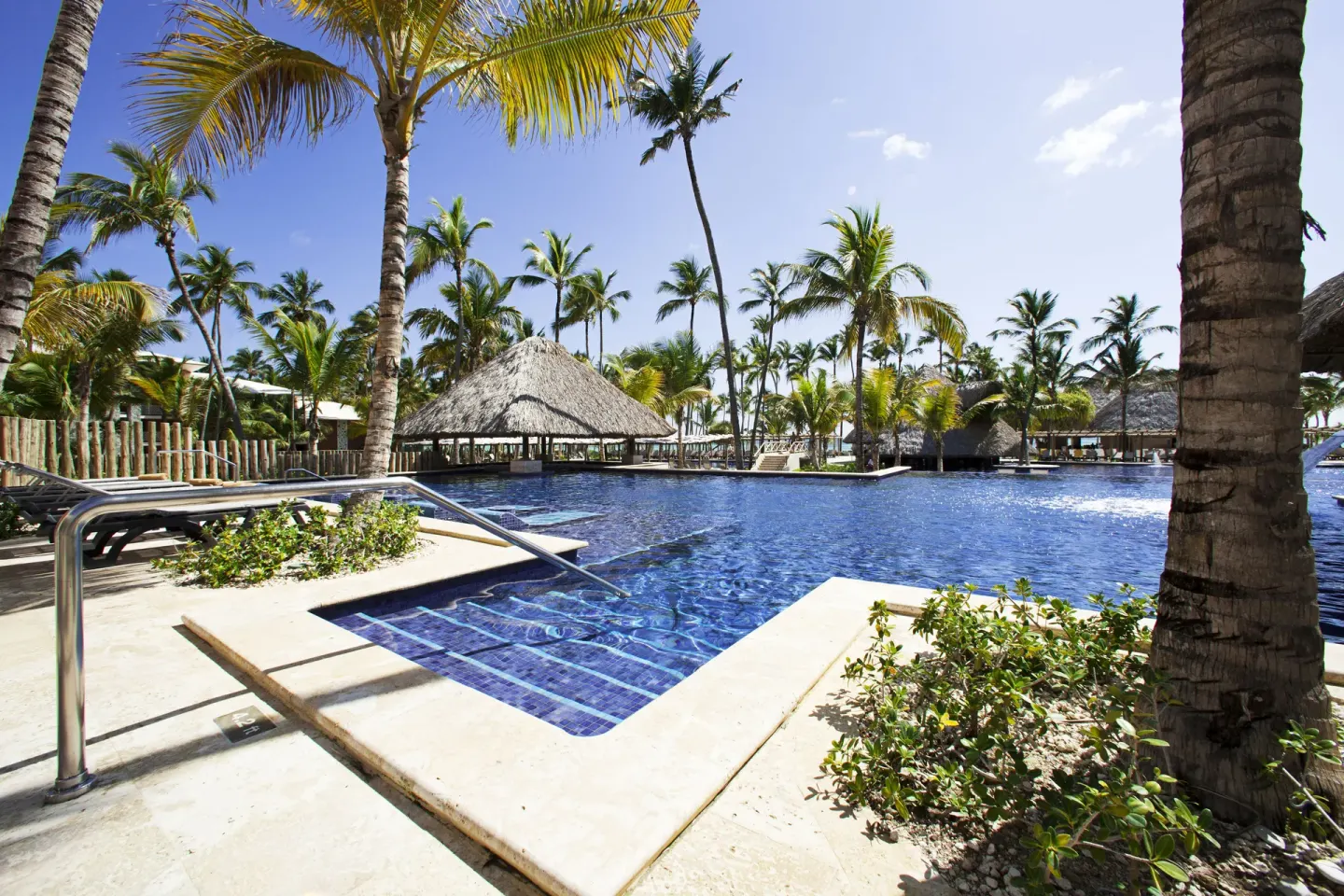 Resort pool with palm trees, loungers, and thatched shade roofs at Barceló Bávaro Palace.