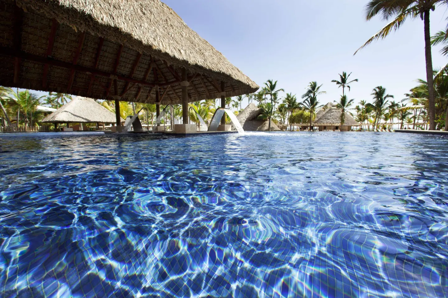 Thatched shade palapas beside the blue resort pool at Barceló Bávaro Palace.